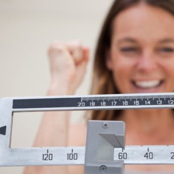 mulher feliz sorridente em frente a uma balança de peso