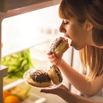 imagem de uma mulher comendo doces em frente a geladeira